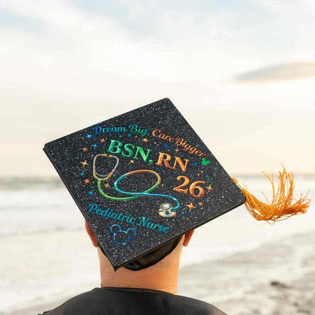 Graduate wearing a 'BSN RN 26' pediatric nurse grad cap topper at the beach