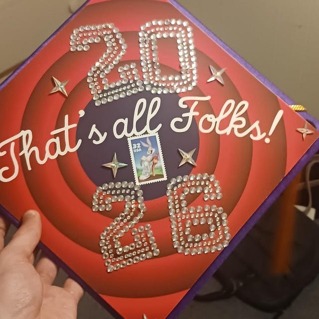 Graduate holding a rhinestone 'That's All Folks 2026' grad cap topper