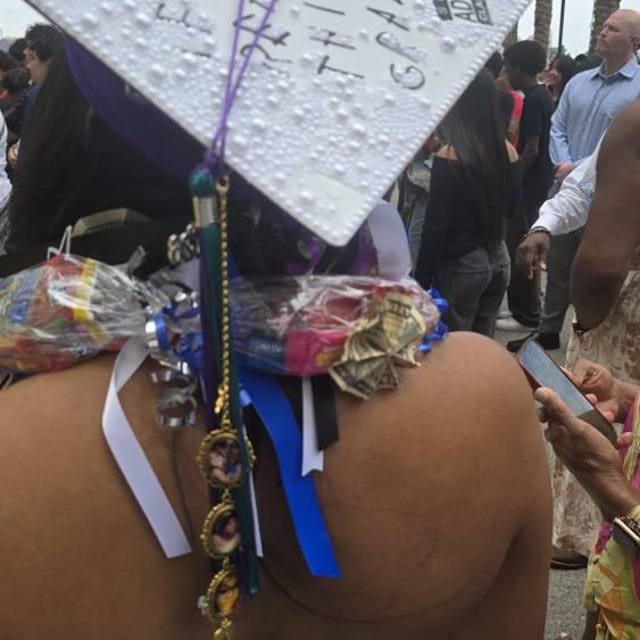 Graduate wearing a white glitter grad cap topper with money leis at commencement