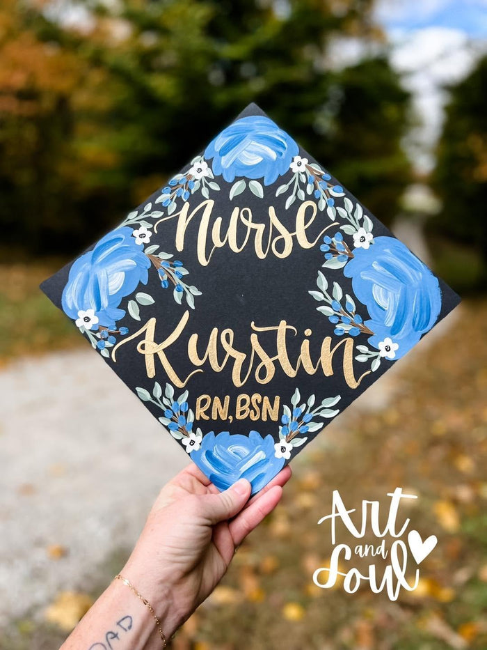 Graduate holding a blue floral 'Nurse Kurstin RN BSN' grad cap topper