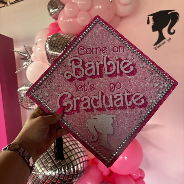 Graduate holding a pink Barbie 'Come On Barbie Let's Go Graduate' grad cap topper