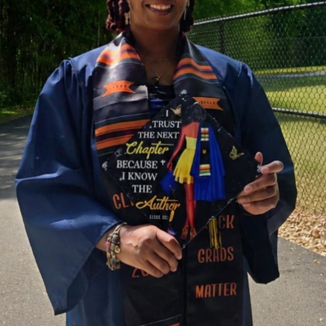 Graduate holding an 'I Trust the Next Chapter Because I Know the Author' grad cap topper