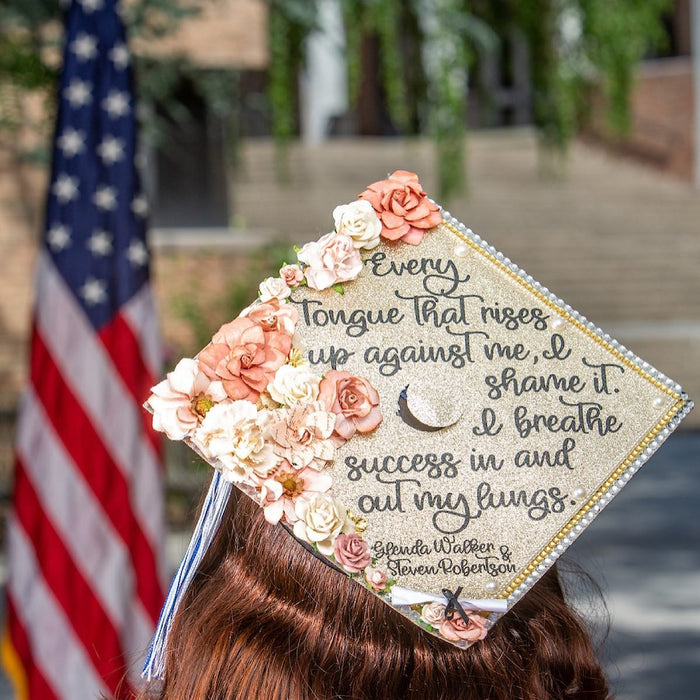 Graduate wearing a floral quote grad cap topper in front of an American flag