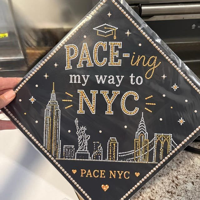 Graduate holding a 'Pace-ing My Way to NYC' Pace University grad cap topper