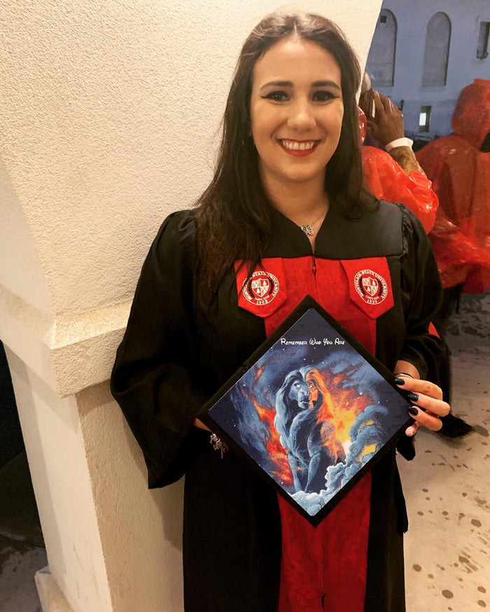 Graduate in a gown holding a blue dragon fantasy grad cap topper