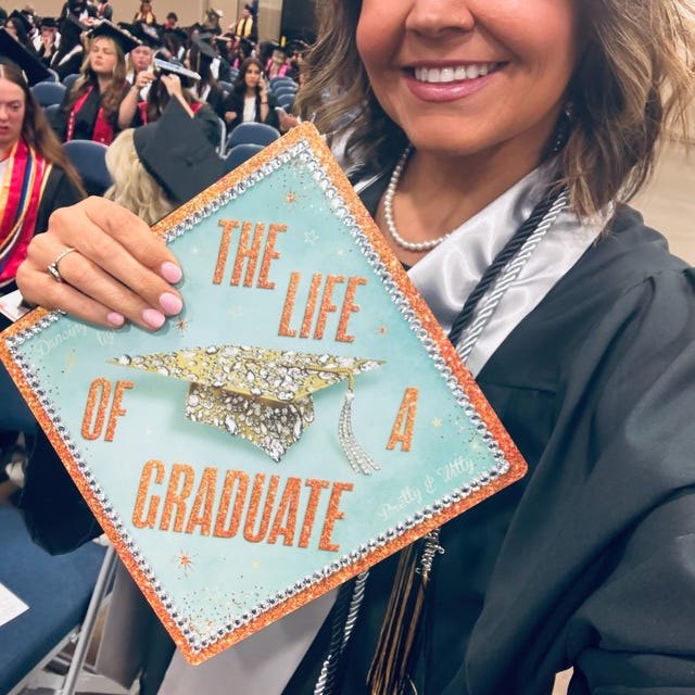 Graduate holding a 'The Life of a Graduate' sparkly grad cap topper at commencement