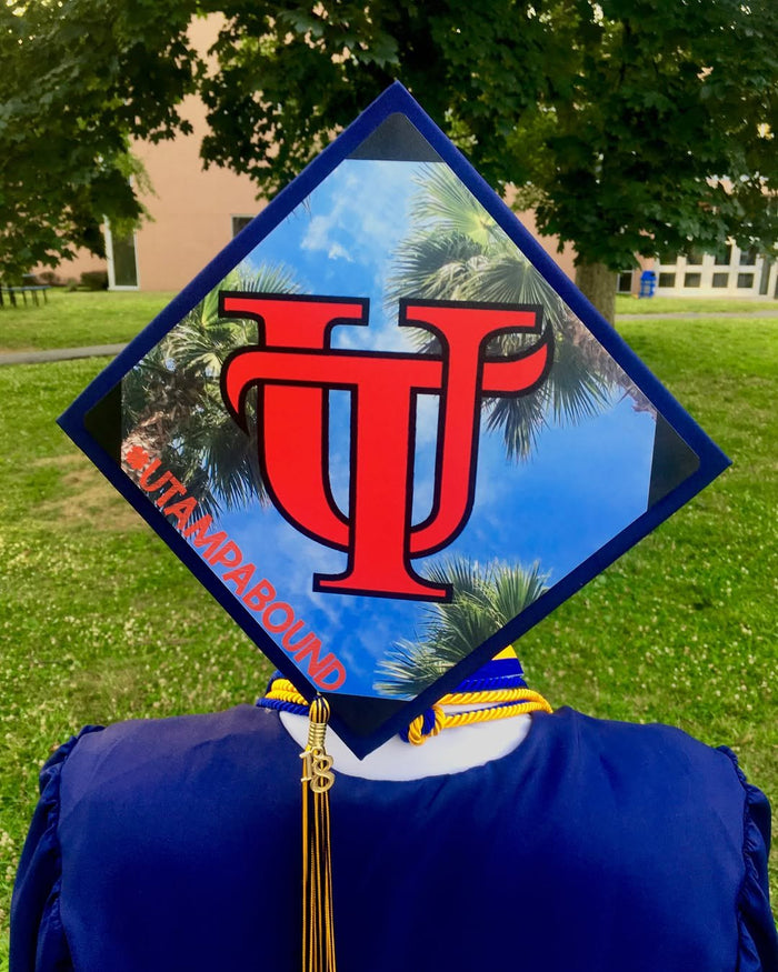 Graduate wearing a University of Tampa logo grad cap topper