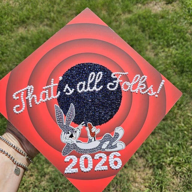 Graduate holding a Bugs Bunny 'That's All Folks 2026' grad cap topper