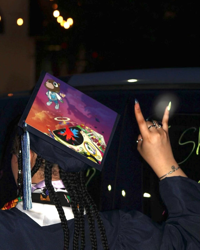 Graduate wearing a Kanye West Graduation bear grad cap topper at night