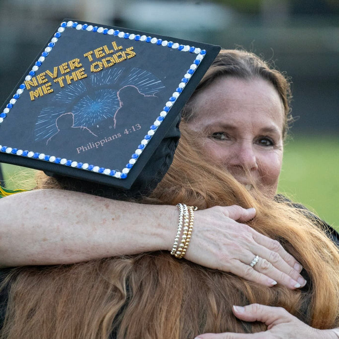 Graduate wearing a Star Wars 'Never Tell Me the Odds' grad cap topper while hugging family