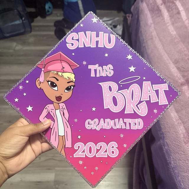 Graduate holding a purple SNHU 'This Brat Graduated 2026' grad cap topper