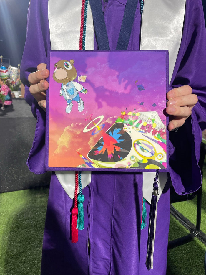 Graduate in purple gown holding Kanye Graduation bear topper