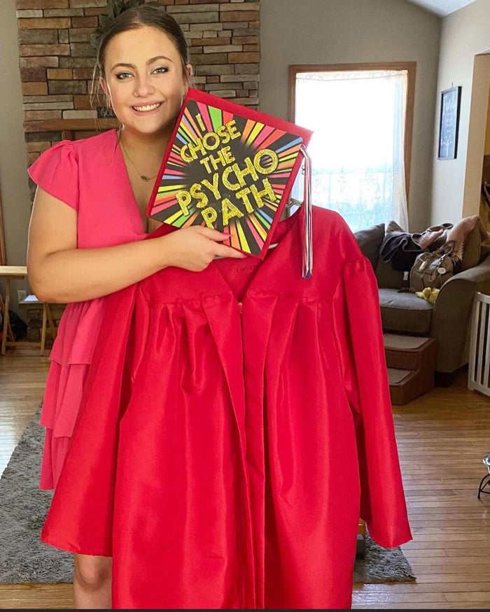 Woman holding I Chose the Psycho Path cap with red gown
