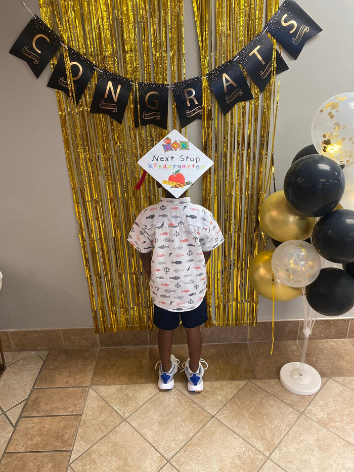Child wearing Next Stop Kindergarten cap at congrats backdrop