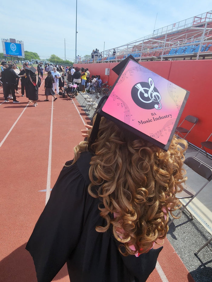 Graduate wearing pink Music Industry cap at stadium, back view