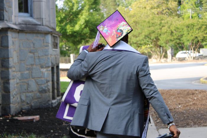 Graduate in suit wearing Kanye bear cap outdoors