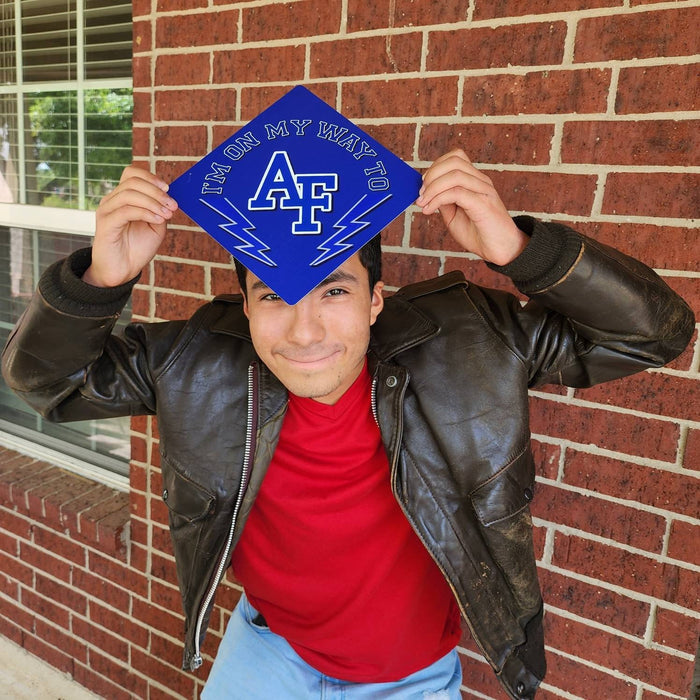 Young man holding Air Force On My Way cap over his head