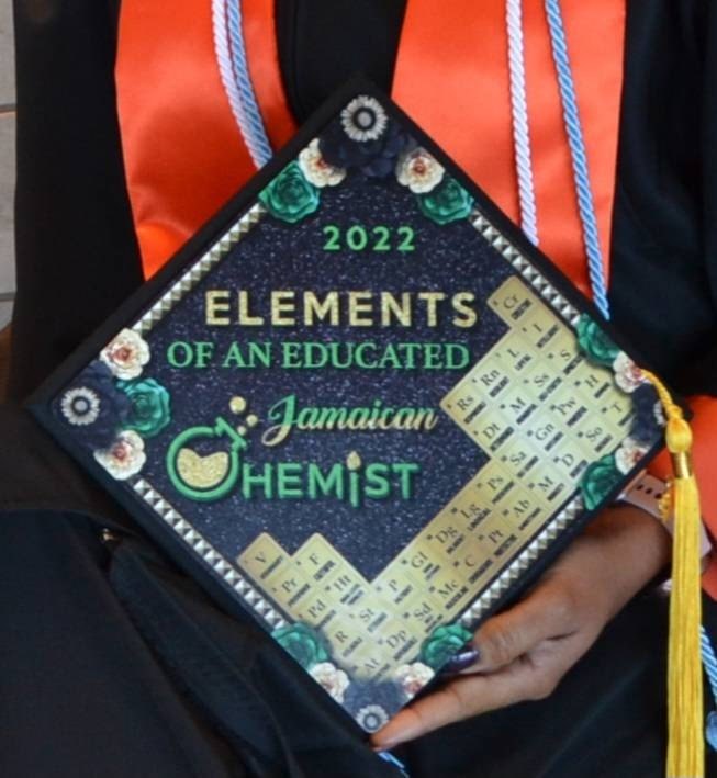 Graduate holding Elements Of An Educated Jamaican Chemist cap