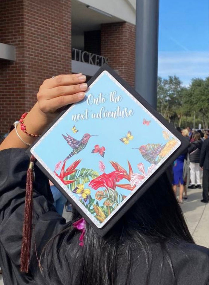 Graduate holding hummingbird Onto The Next Adventure cap