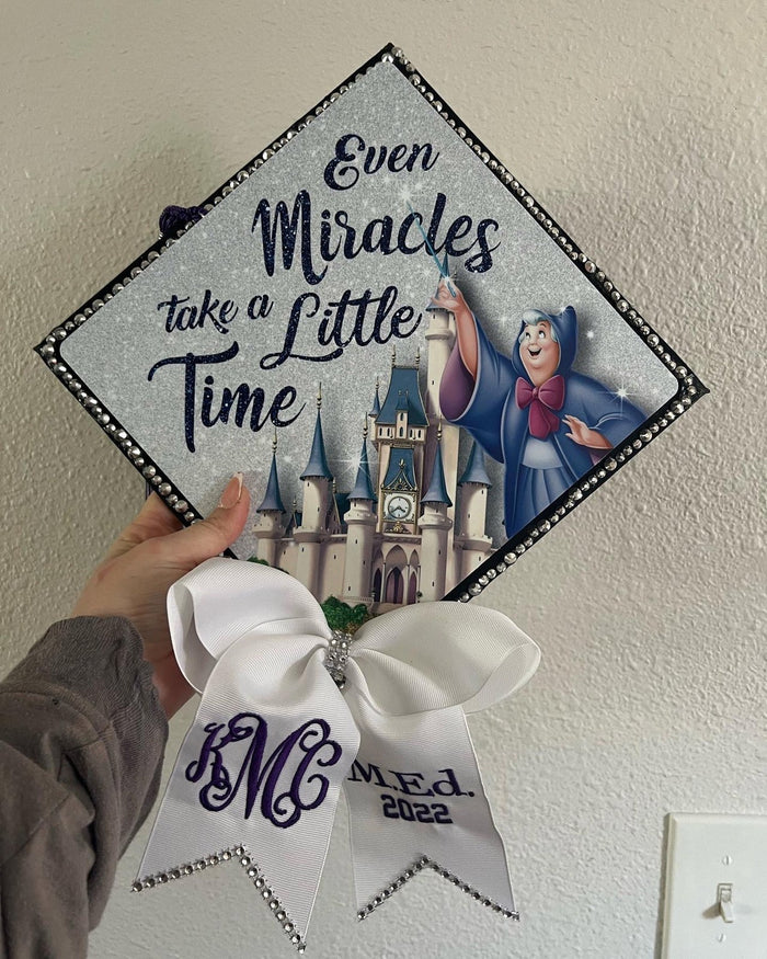 Hand holding Cinderella Even Miracles Take A Little Time cap