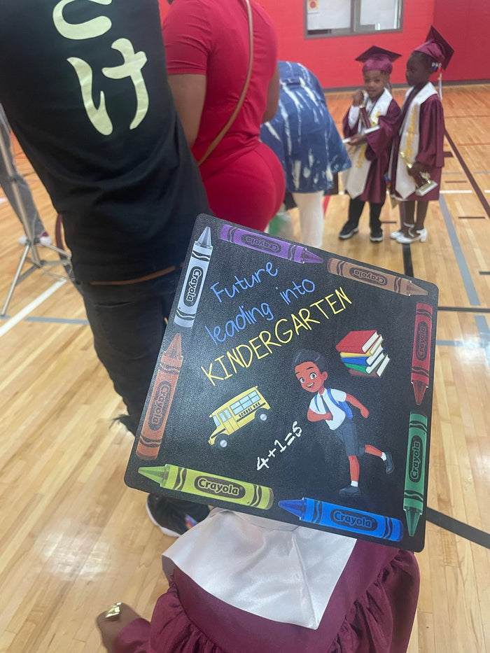Child graduate scene holding Future Kindergarten crayon topper in gym