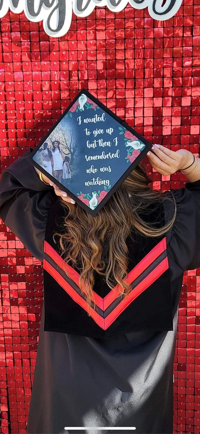 Graduate holding cap up against red sequin wall