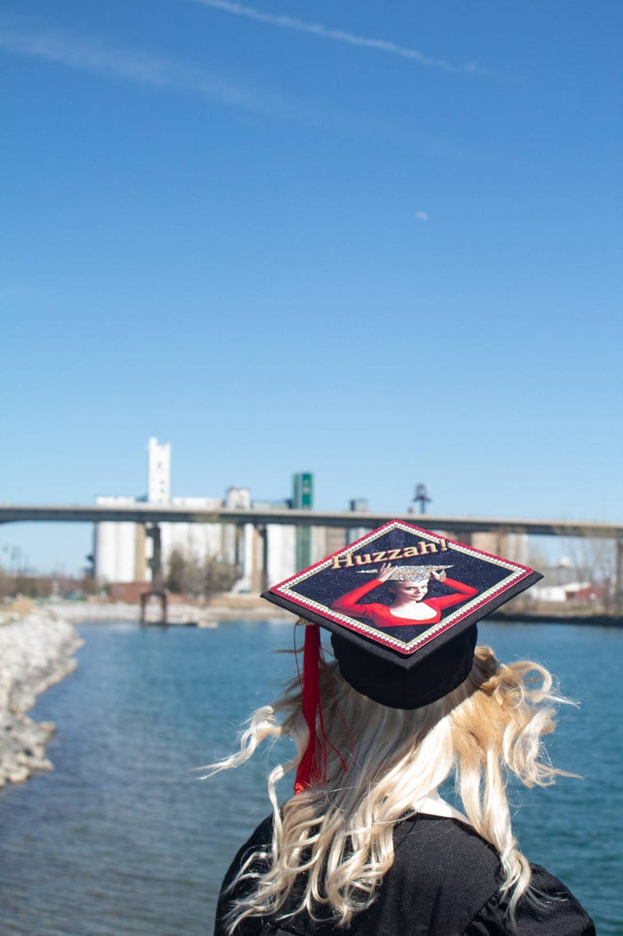 Graduate wearing Huzzah Greatest Showman cap by river