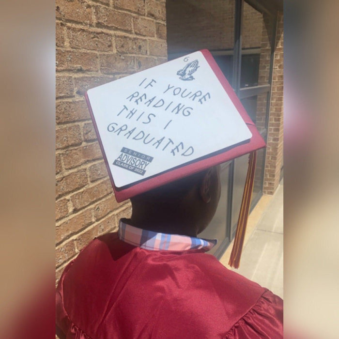 Graduate in red gown wearing If Youre Reading This cap, back view