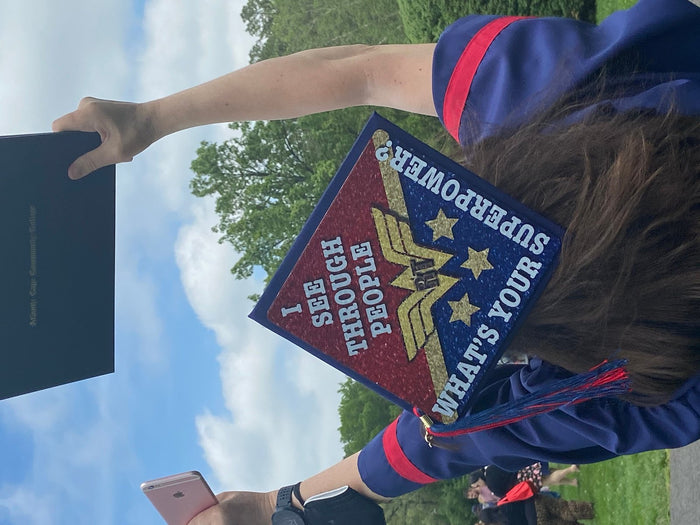 Graduate holding Wonder Woman Whats Your Superpower cap to sky