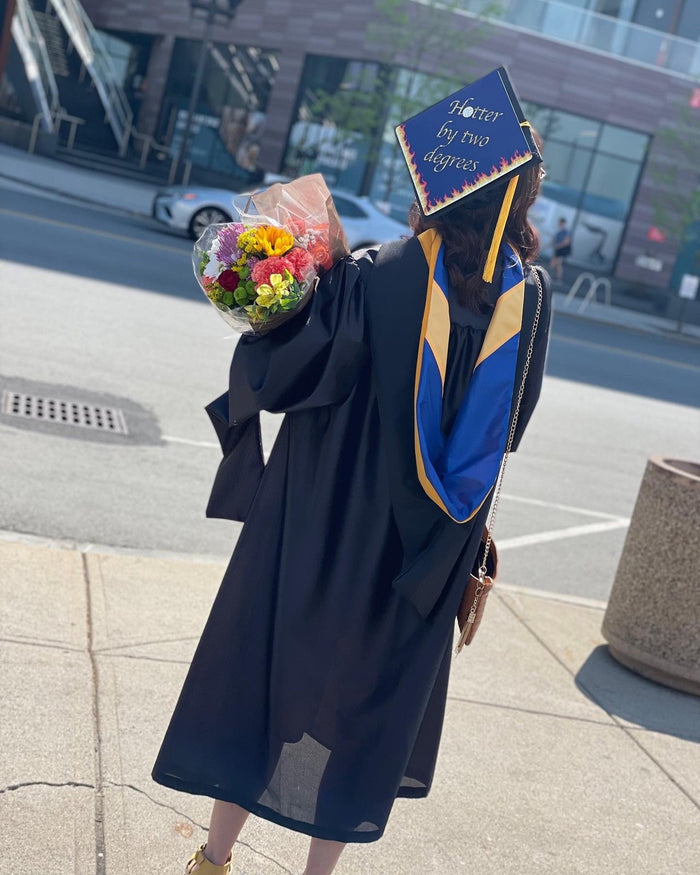 Graduate wearing Hotter By Two Degrees cap holding flowers