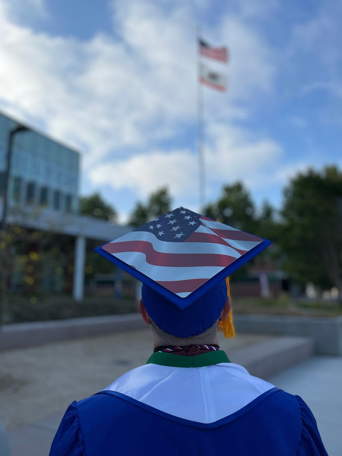 Graduate wearing US flag cap on campus, back view