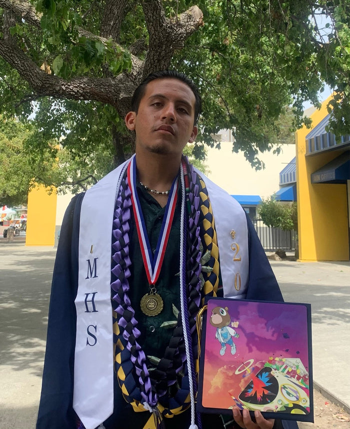 Graduate with medals holding Kanye topper