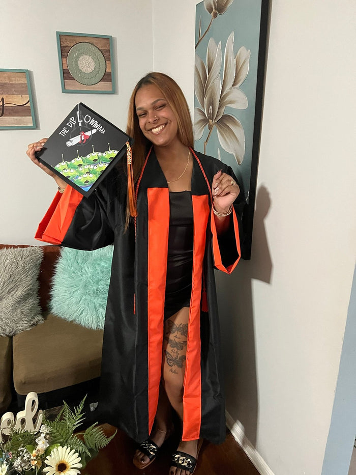 Graduate in gown holding decorated cap indoors