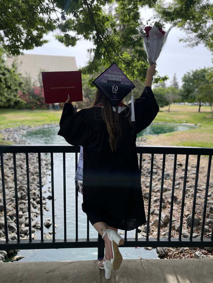 Graduate wearing Breaking Generational Curses cap with diploma by pond