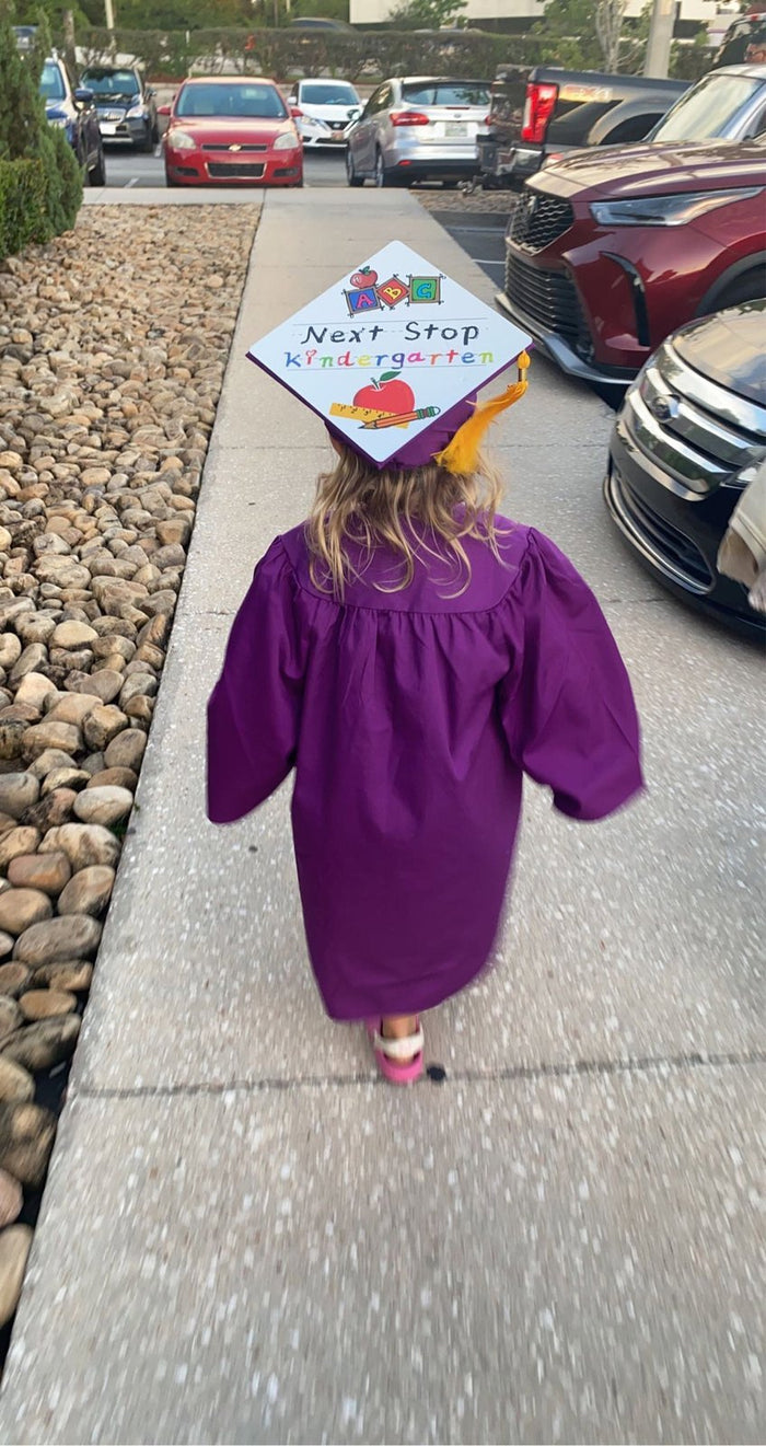 Child in purple gown wearing Next Stop cap in parking lot