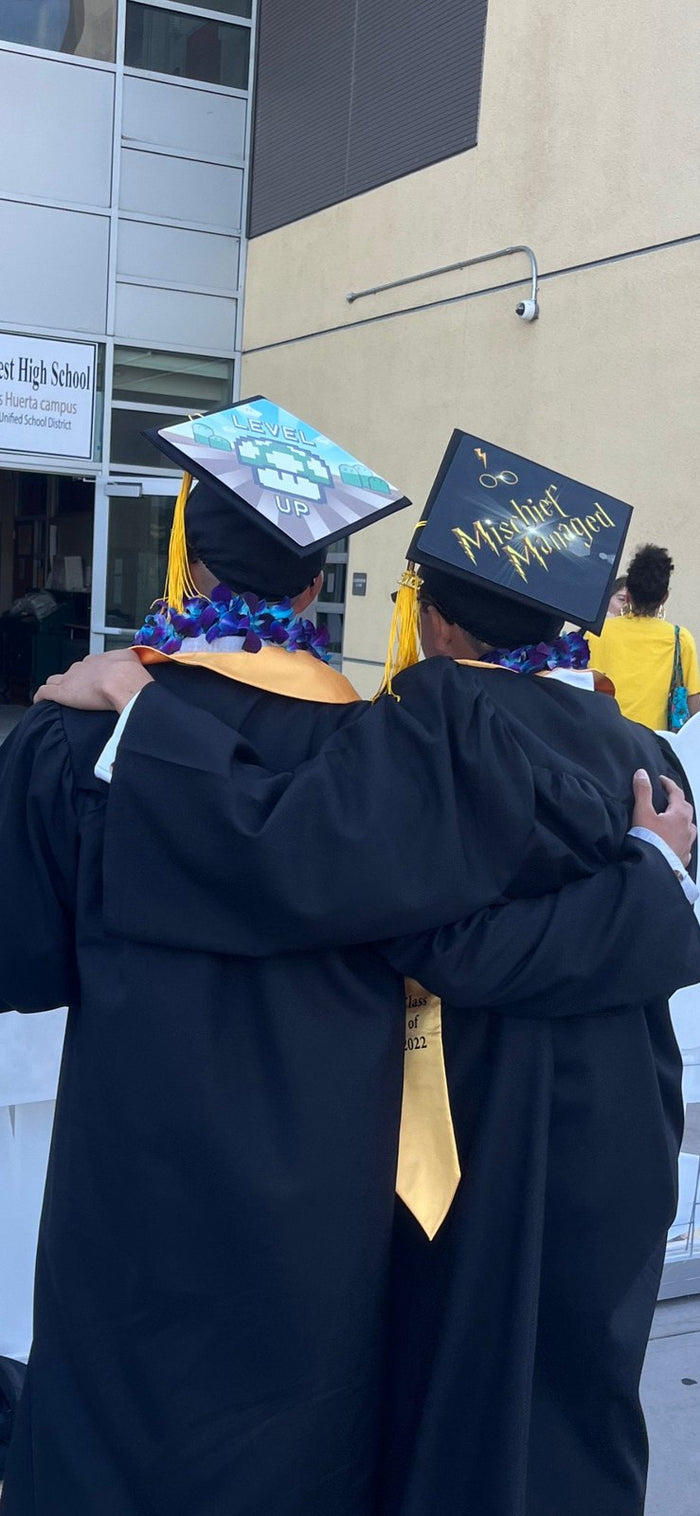 Two graduates wearing Level Up and Mischief Managed caps