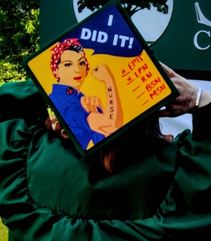 Graduate in green gown holding Rosie I Did It nurse cap