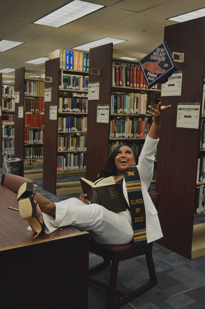 Graduate tossing Run Me My Degree cap in library