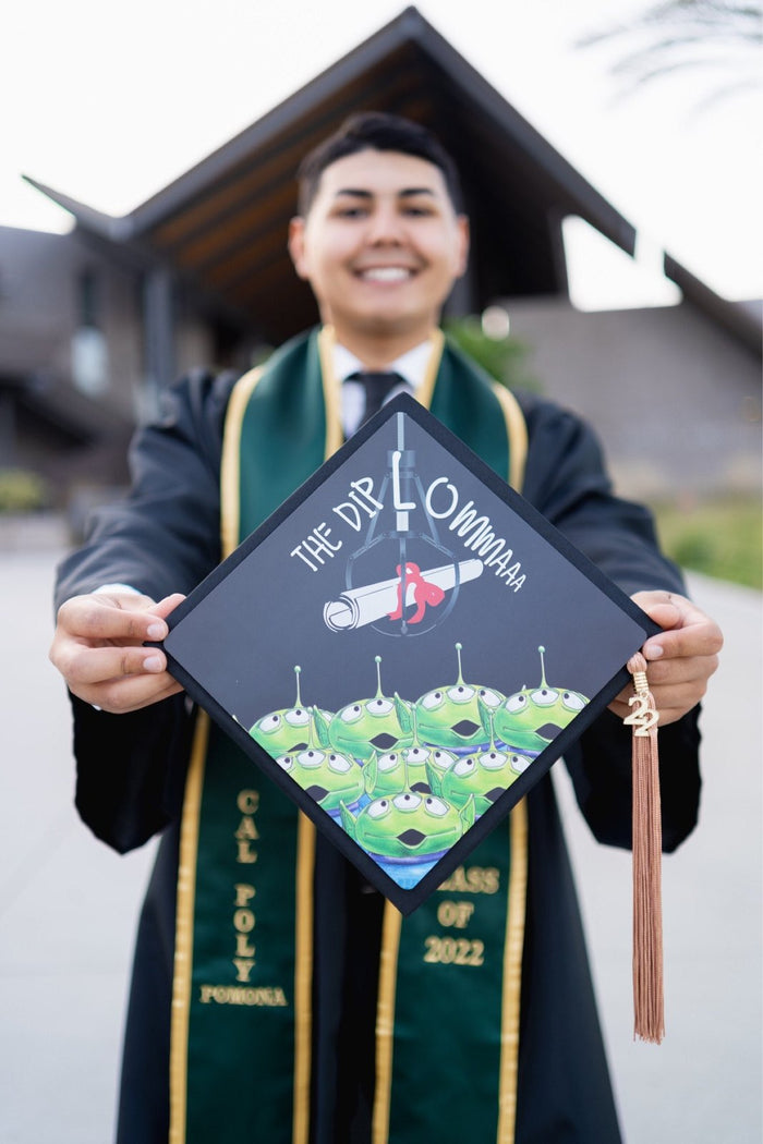 Graduate holding Toy Story aliens The Diplowmaaa cap