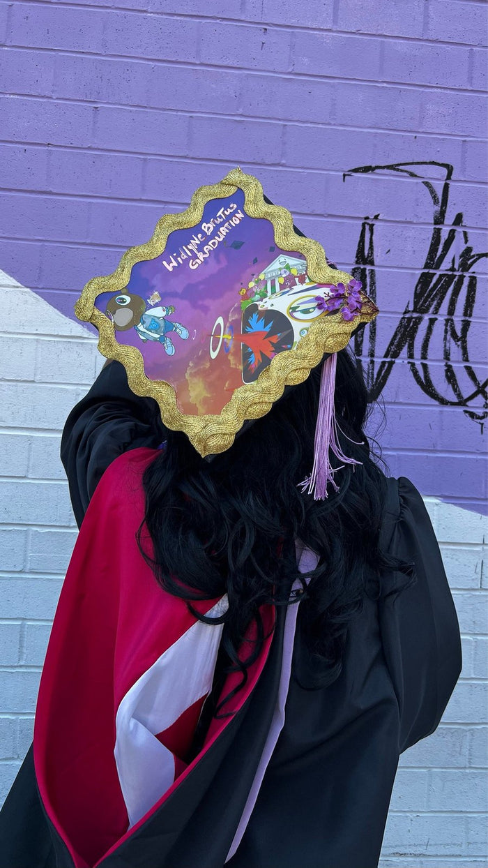 Graduate wearing Encanto style cap by purple wall, back view