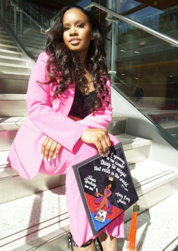 Woman in pink suit holding decorated cap on stairs