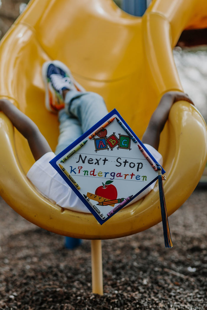 Child wearing Next Stop Kindergarten cap on playground slide