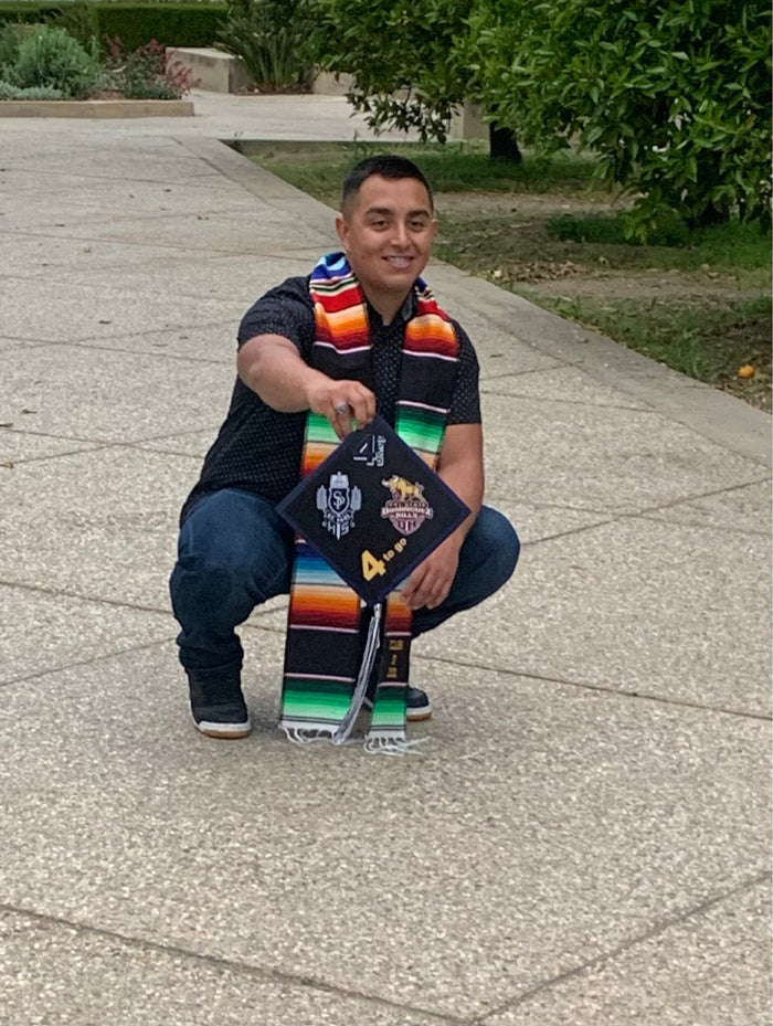 Graduate crouching holding 4 To Go Dominguez Hills cap