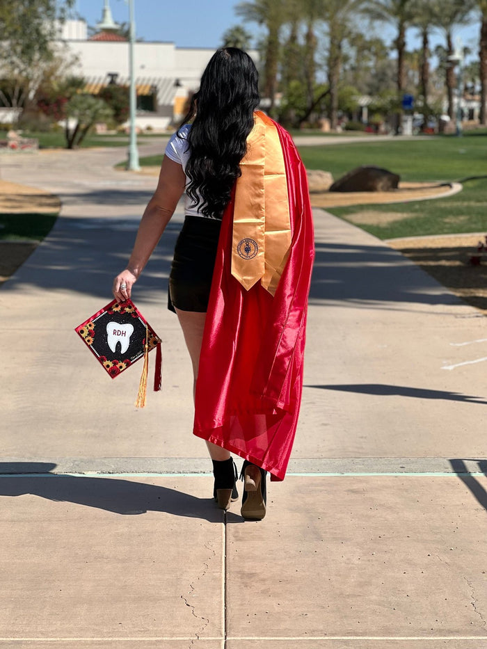 Graduate holding RDH tooth sunflower cap on campus walk