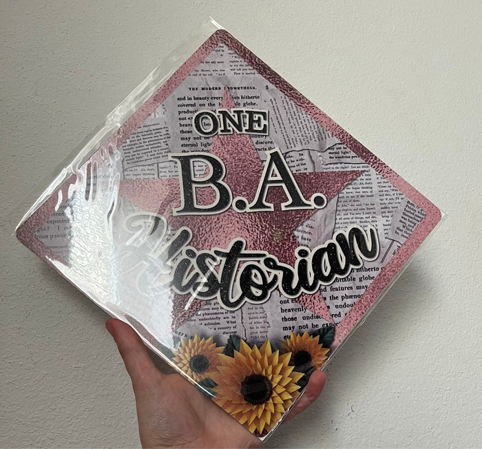 Hand holding One BA Historian newspaper topper