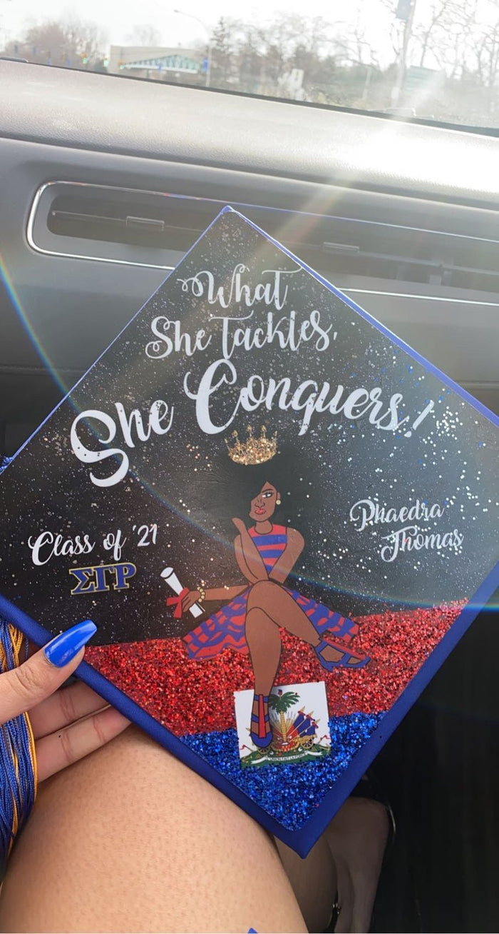 Hand holding What She Tackles She Conquers Haiti topper in car