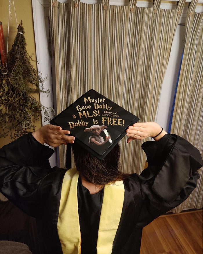 Graduate holding Dobby Is Free MLS cap over head