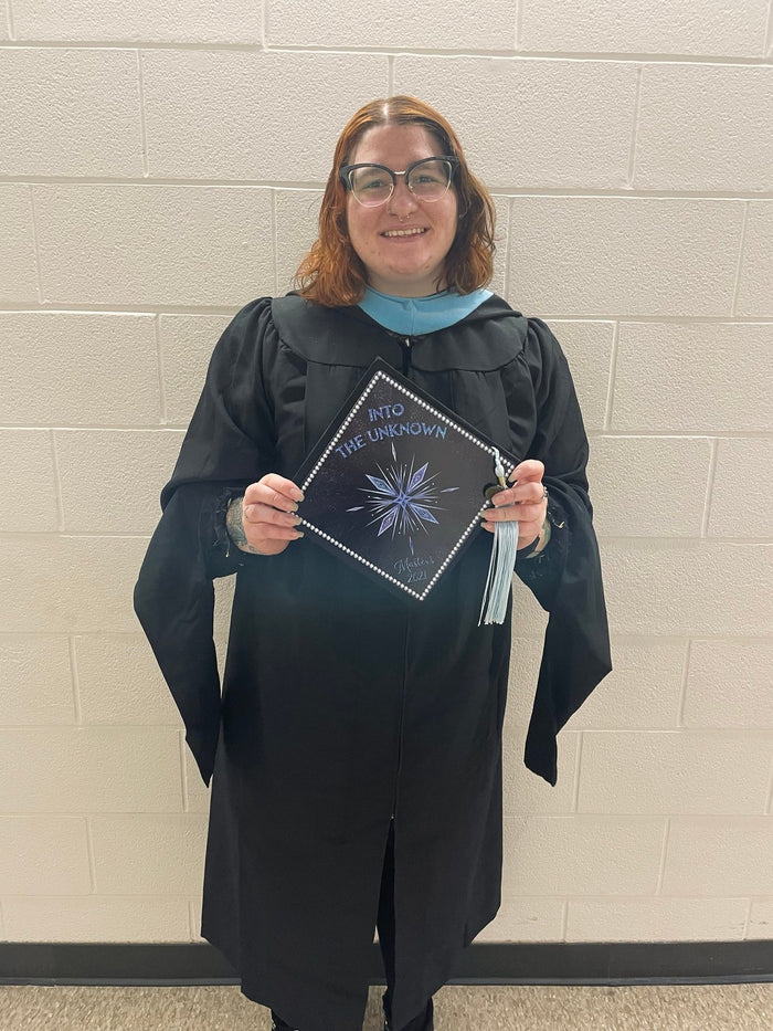 Graduate in gown holding compass star topper in hallway