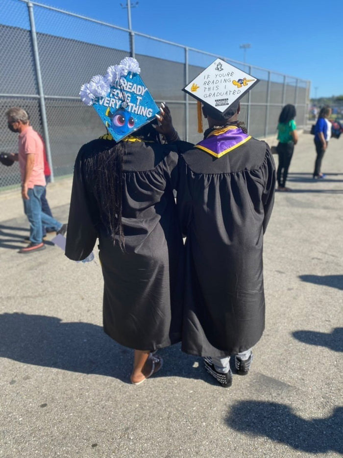 Two graduates walking wearing Dory and If Youre Reading This caps