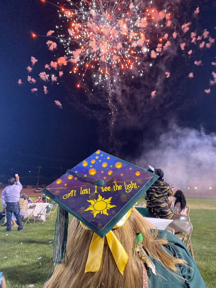 Graduate wearing Tangled At Last I See The Light cap at fireworks